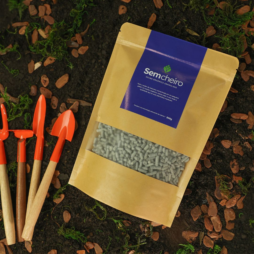 Adubo orgânico Sem Cheiro 500g com ferramentas de jardinagem sobre terra com cascas e musgo